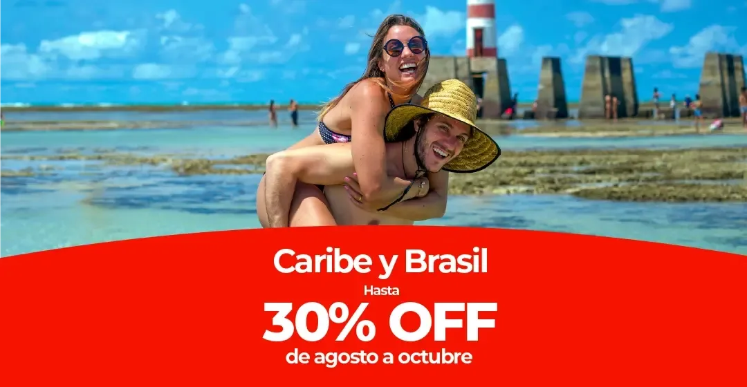 Pareja sonriente en aguas poco profundas, mujer sobre hombre, faro detrás.