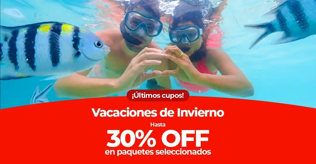 Una pareja buceando entre peces en el océano, haciendo un corazón con las manos.