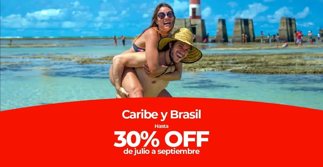 Pareja en el agua poco profunda de la playa con un faro al fondo.
