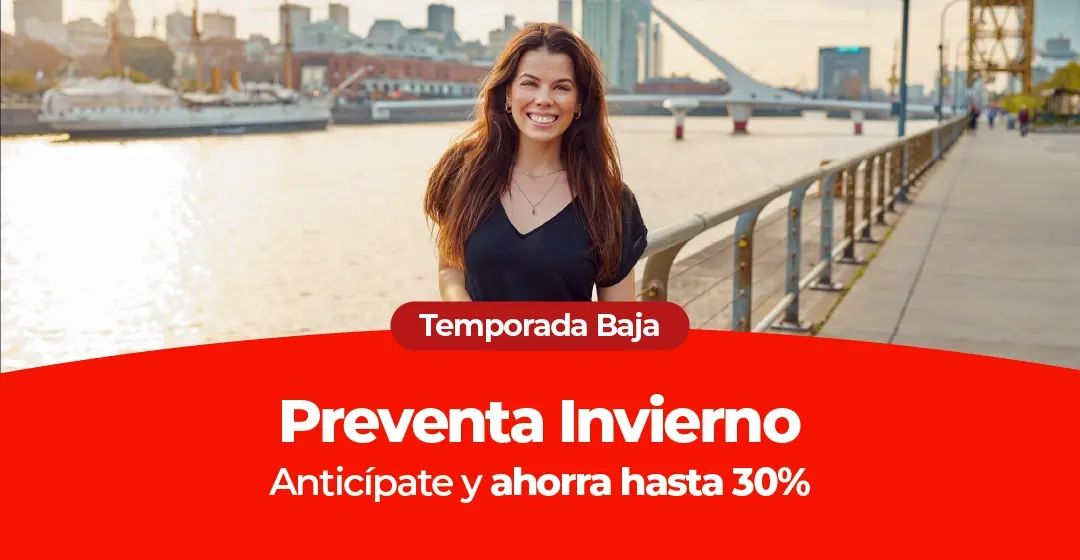 Una mujer sonriente en un paseo ribereño con la ciudad y un puente al fondo.
