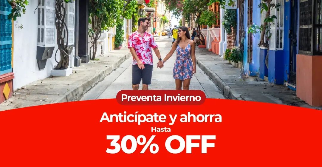 Pareja camina de la mano por una calle con edificios coloridos y vegetación.