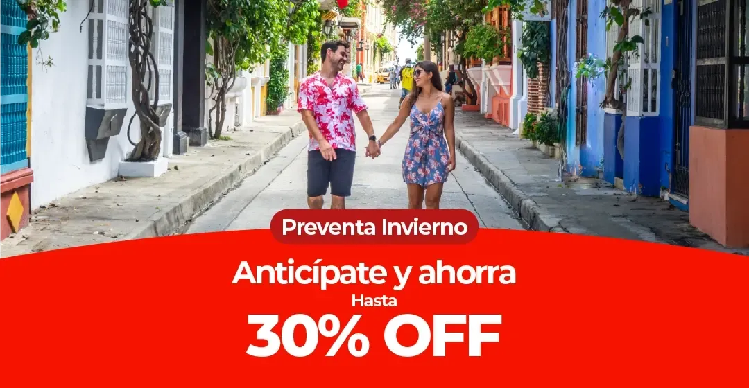 Pareja camina de la mano por una calle con edificios coloridos y vegetación.