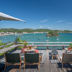 Deck con asientos y mesas sobre una bahía con botes y pueblo.