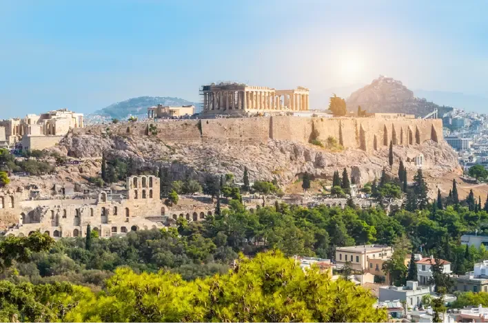 Vista del Partenón y la Acrópolis sobre Atenas con ruinas antiguas y árboles.