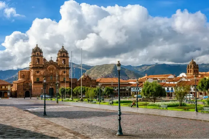 Iglesia de la Compañía de Jesús en plaza de Cusco con montañas.