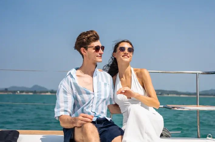 Pareja con gafas de sol sentada en un barco con el mar de fondo.