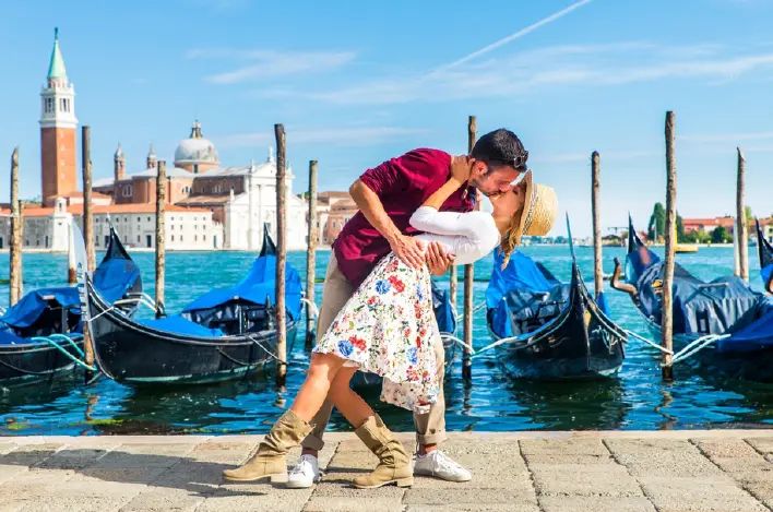 Un hombre y una mujer se besan frente a góndolas en Venecia.