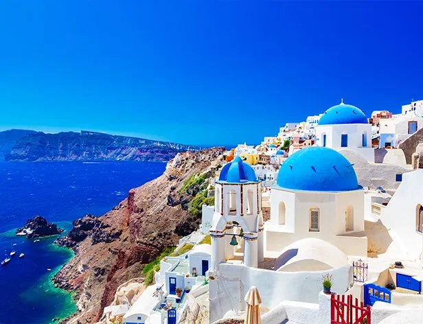 Pueblo costero con edificios blancos de cúpulas azules y el mar.