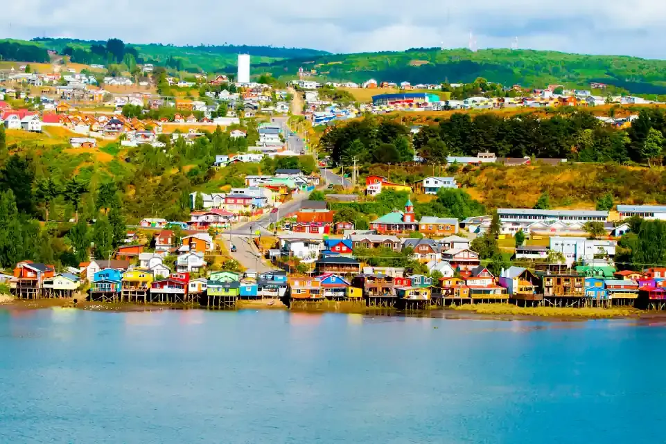 Pueblo con casas coloridas en ladera y palafitos junto al agua.