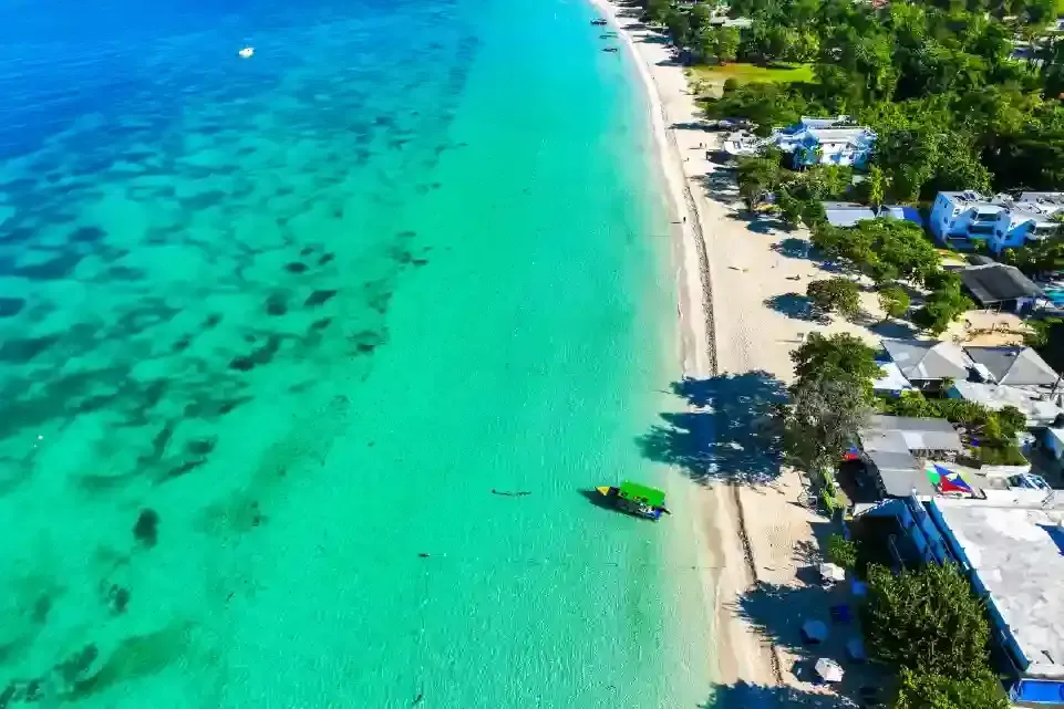 Vista aérea de una playa con edificios, océano y un barco cerca de la orilla.