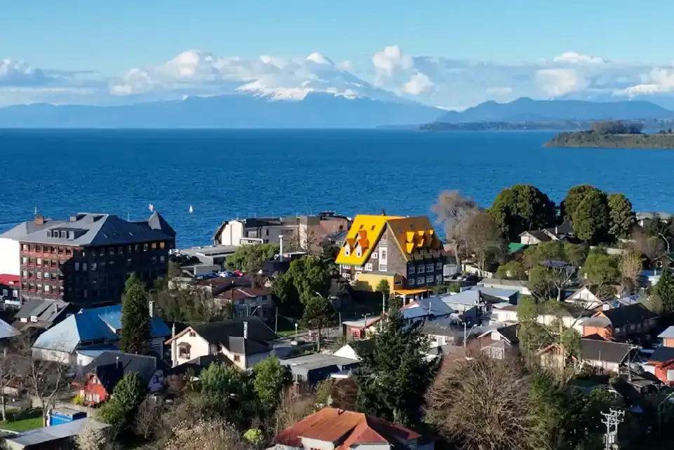 Un pueblo junto a un lago con montañas nevadas de fondo.