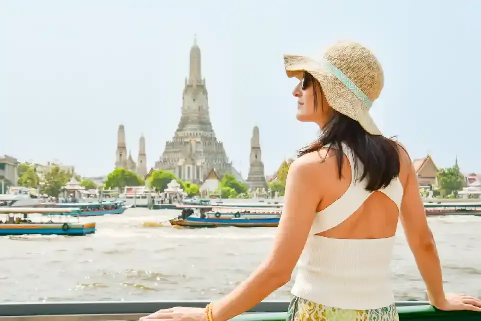 Una mujer con sombrero de paja observa el templo Wat Arun desde el río.