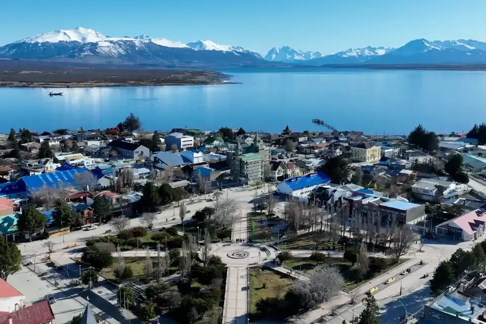 Vista aérea de un pueblo con plaza central, lago y montañas nevadas.