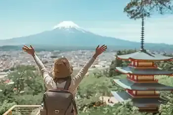 Una persona de espaldas con brazos alzados frente al Monte Fuji y una pagoda.