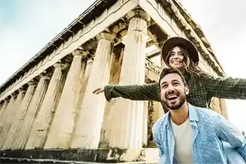 Un hombre y una mujer sonrientes posan frente a un templo antiguo con columnas.